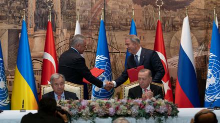 Antonio Guterres (vorn l), UN-Generalsekretär, und Recep Tayyip Erdogan (r), Präsident der Türkei, sitzen während einer Unterzeichnungszeremonie im Dolmabahce-Palast, während sich zwei Vertreter der Delegationen der Ukraine und Russlands die Hände reichen.