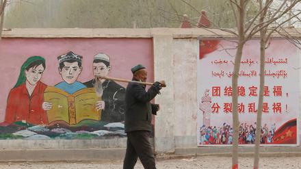 Mandarin verdrängt Uigurisch. Ein Bauer in der Nähe von Kashgar in Xinjiang passiert propagandistische Wandbilder, die ethnische Minderheiten mit dem Slogan «Einheit, Stabilität ist Glück, Separatismus und Unruhe sind Unglück» dazu auffordern, die Verfassung ui lesen.