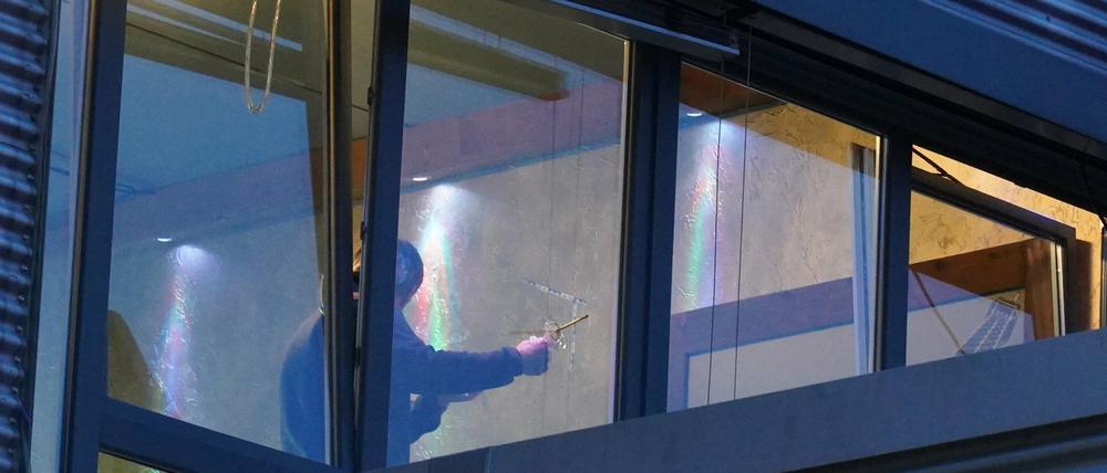 Ein Ermittler untersucht ein Einschussloch in einer Fensterscheibe. Der oder die Täter hätten mit einer unbekannten Waffe noch ein weiteres Fenster in dem Gebäudekomplex beschossen.