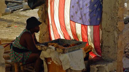 Eine Frau verkauft im Mai 2010 in Port-au-Prince, Haiti, gebackene Bananen und sitzt neben einer US-Nationalflagge.