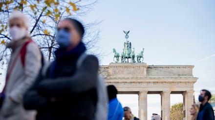 Menschen mit Mund-Nasen-Bedeckungen stehen vor dem Brandenburger Tor.