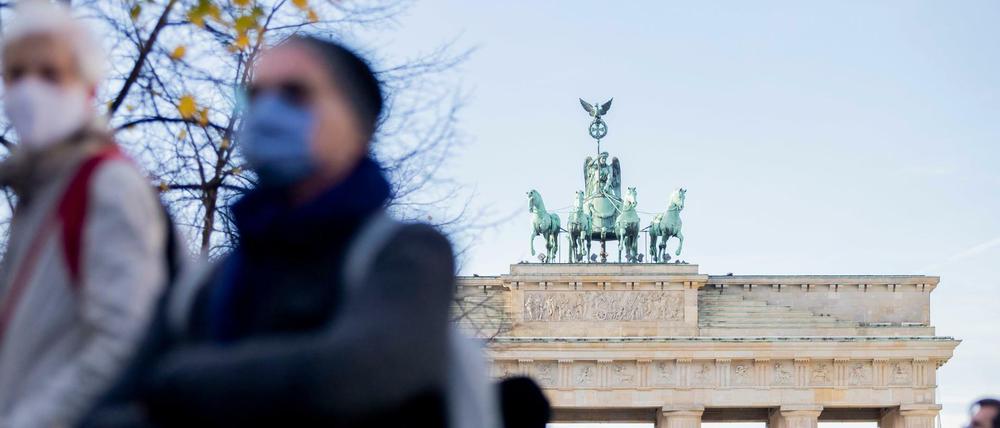 Menschen mit Mund-Nasen-Bedeckungen stehen vor dem Brandenburger Tor.