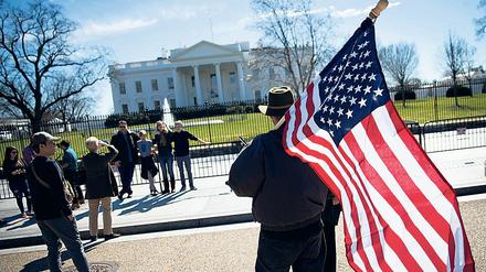 Ein Mann mit USA-Flagge vor dem Weißen Haus in Washington.