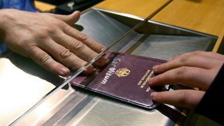 Ein Deutscher Pass wird bei einer Passkontrolle unter einer Scheibe durchgereicht. 
