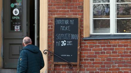 Ein Schild mit der Aufschrift "Eintritt nur mit Maske Sitzplätze innen mit 2G Genesen oder Geimpft" ist in der Potsdamer Innenstadt neben dem Eingang zu einem Café angebracht.