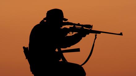 Ein Jäger sitzt bei Sonnenuntergang mit angelegtem Gewehr auf einem Hochstand unweit der brandenburgischen Ortschaft Fürstenwalde.