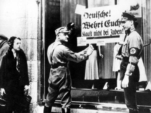 Was in Deutschland begann, griff auch auf andere Länder Europas über. SA-Männer kleben ein Plakat mit der Aufschrift "Deutsche! Wehrt Euch! Kauft nicht bei Juden" an die Schaufensterscheibe eines Geschäfts, das in jüdischem Besitz ist (undatiertes Archivfoto). 