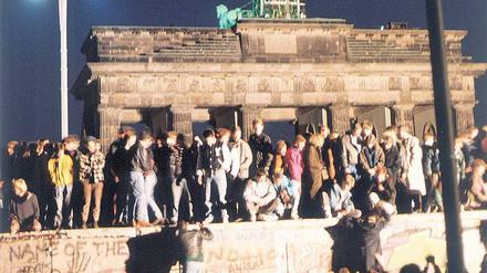 Bild voller Symbolkraft. Feiernde Menschen auf der Berliner Mauer vor dem Brandenburger Tor am 9. November 1989.