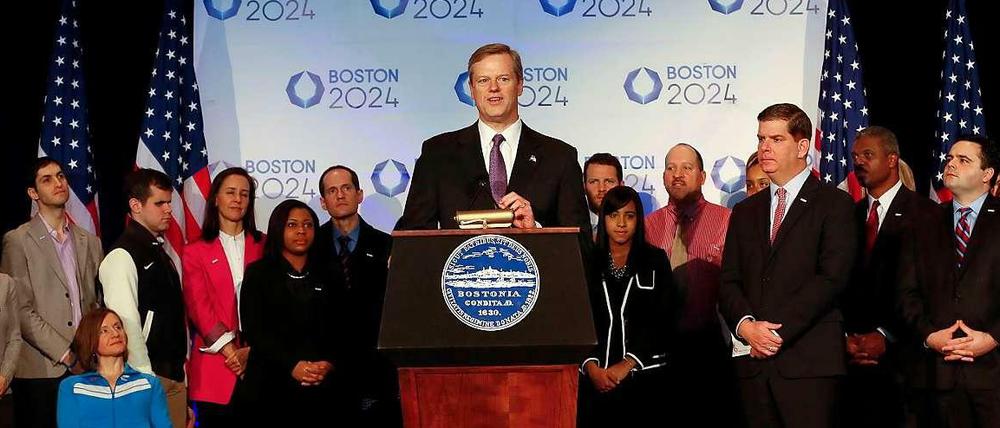 Charlie Baker, Governor von Massachusetts, steht bei der offiziellen Pressekonferenz zur Olympiabewerbung von Boston an einem Pult mit einem guten Dutzend weiterer Representanten in seinem Rücken.
