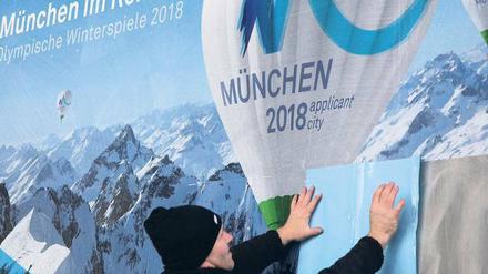 Kleben für Olympia. Ein Helfer befestigt das Logo der Münchner Bewerbung für die Winterspiele 2018 auf einen Plakatträger. Foto: dpa