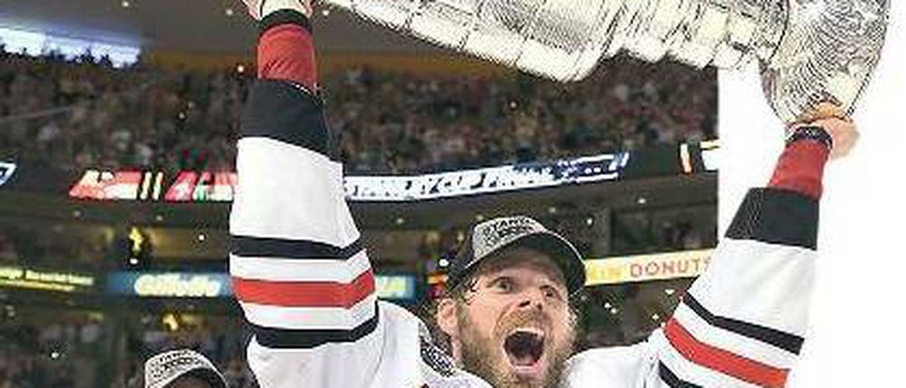 Potthässlich, aber sehr begeht. Chicagos Michal Handzus stemmt den schweren Stanley Cup in die Höhe, nachdem er ihn von Kapitän Jonathan Toews (l.) bekommen hat. Foto: AFP