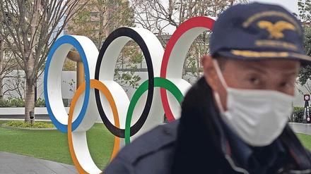 Die Spiele und das Virus. Ein Sicherheitsbeamter geht in der Nähe des neuen Nationalstadions in Tokio an den Olympischen Ringen vorbei.
