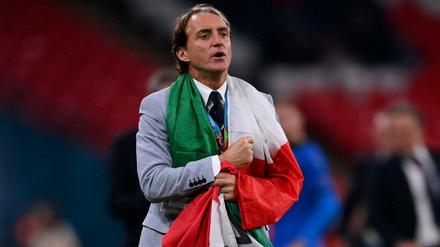 Italiens Trainer Roberto Mancini geht über den Platz, eingehüllt in eine Italienflagge.