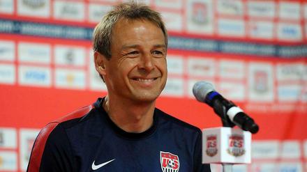 Jürgen Klinsmann sitzt grinsend auf einer Pressekonferenz