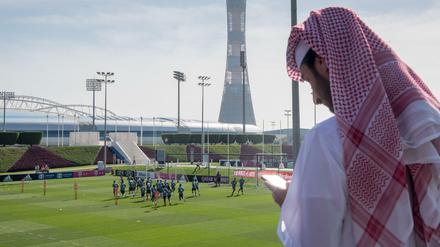 Ein Mann schaut in Doha auf sein Handy, während die Fußballer von Bayern München trainieren.