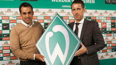 Robin Dutt (l.) und  Thomas Eichin halten das Logo von Werder Bremen.