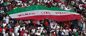Iranische Fans halten auf der Tribüne eine Flagge mit der Aufschrift „Woman Life Freedom“ hoch.