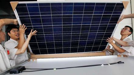 Chinesische Arbeiter verpacken ein großes viereckiges Solarpanel.