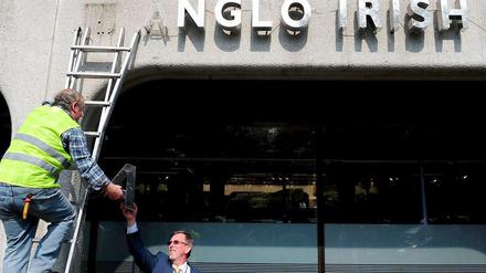 Ein Mann auf einer Leiter demontiert den Schriftzug der bankrotten Anglo Irish Bank. 