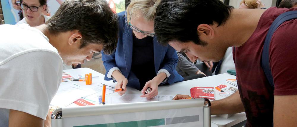 Auf einer Ausbildungsmesse für Flüchtlinge hilft Ulrike Nennhaus (M) vom Jobcenter Schwerin beim Ausfüllen von Formularen. 