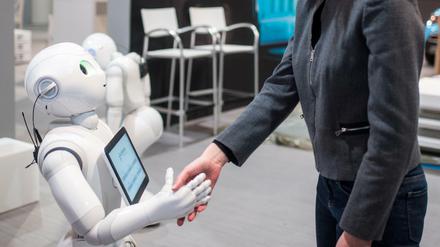 Die Kommunikationsmanagerin von Aldebaran, Aurora Chiquot, schüttelt auf dem Messegelände der CeBIT Hannover am Stand von Aldebaran dem humanoiden Roboter "Pepper" die Hand.