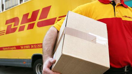 Ein Mitarbeiter des Paketdienstleisters DHL der Deutschen Post trägt ein Paket (Symbolbild).