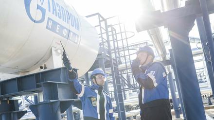 Mitarbeiter stehen an einem Tank, auf dem das Logo der Firma Gazprom zu sehen ist. 