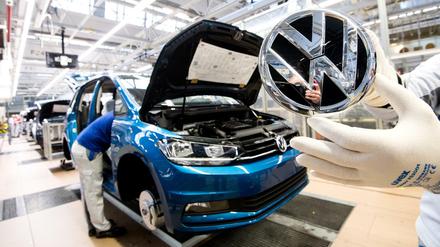 Ein VW-Mitarbeiter zeigt das Markenlogo kurz vor Einbau in einen Volkswagen Touran in der Endmontage im VW Werk. (Archivbild 2019)