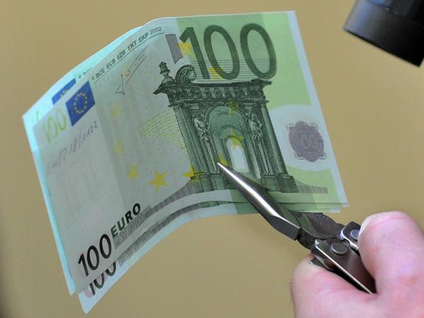 Ein Polizist hält Falschgeld mit einer Zange. Im Wettlauf mit Geldfälschern legen Europas Währungshüter nun nach. (Archivbild)