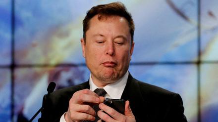 Elon Musk schaut bei einem Gespräch auf sein Smartphone. 