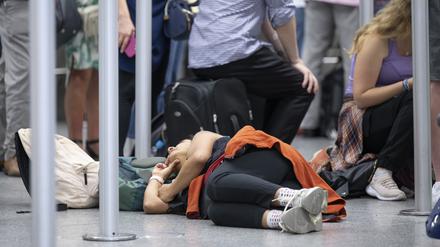 In einer Warteschlange vor einem Check-in-Schalter ruht sich eine Frau, auf dem Boden liegend, aus. Angesichts des Ferienbeginns in mehreren Bundesländern rechnet Flughafenbetreiber Fraport mit einem Rekordansturm.