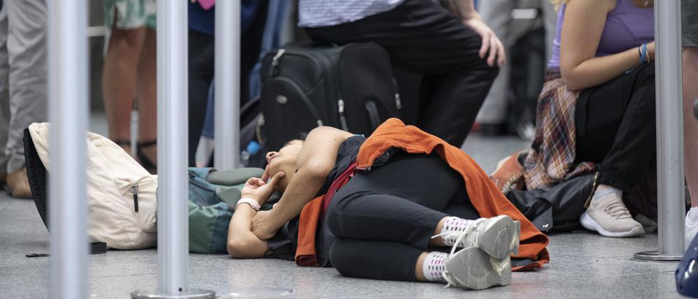 In einer Warteschlange vor einem Check-in-Schalter ruht sich eine Frau, auf dem Boden liegend, aus. Angesichts des Ferienbeginns in mehreren Bundesländern rechnet Flughafenbetreiber Fraport mit einem Rekordansturm.
