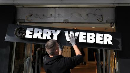 Ein Monteur hängt ein Schild an einer geschlossenen Filiale der Modemarke "Gerry Weber" ab. 