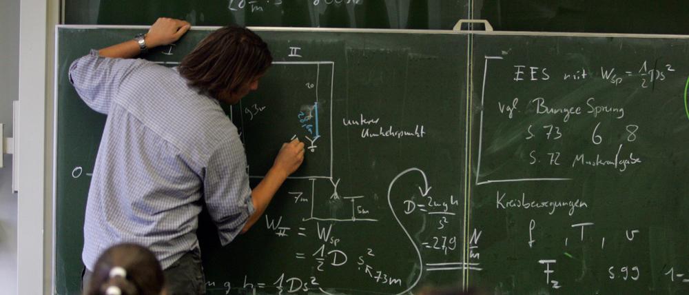 Ein Lehrer schreibt im Physik-Unterricht Formeln an die Tafel, Symbolbild.