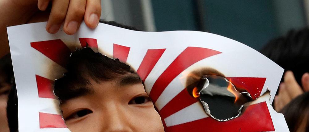 Ein Mann hält ein brennendes Bild der japanischen "Flagge der aufgehenden Sonne" während einer Kundgebung in Seoul. 