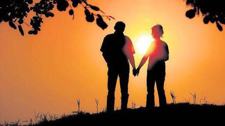 Ein Mann und eine Frau stehen Hand in Hand vor einem Sonnenuntergang.