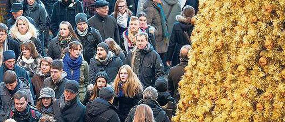 Viele Menschen drängeln sich in einer Einkaufsstraße an einem goldenen Kunstweihnachtsbaum vorbei