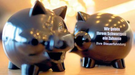 Zwei schwarze Sparschweine. Auf dem einen steht: "Wir geben Ihrem Schwarzgeld ein Zuhause. Ihre Steuerfahndung". 