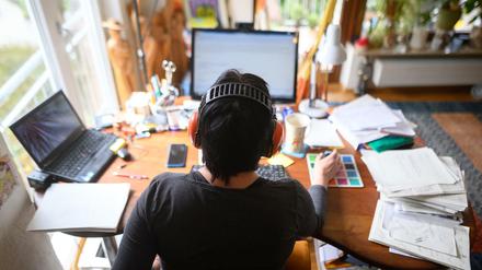 Eine Frau arbeitet mit Hörschutz an einem Schreibtisch mit Laptop und Desktop im Homeoffice.