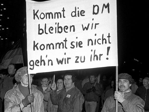  «Kommt die DM bleiben wir kommt sie nicht geh'n wir zu ihr!» ist auf einem Transparent zu lesen, das ein Paar bei einer Montagsdemonstration am 12.2.1990 in Leipzig mit sich führt. 