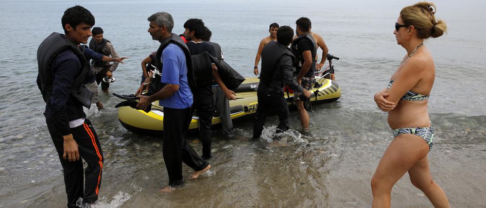 Eine spanische Touristin läuft vorbei, als Flüchtlinge aus Pakistan am Strand der griechischen Insel Kos ankommen.