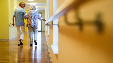 Eine Pflegekraft geht in einem Pflegeheim mit einer älteren Dame über einen Korridor. 