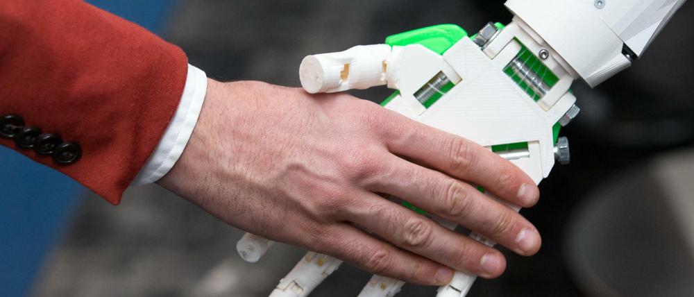 Ein humanoider Roboter gibt einem Menschen die Hand am Stand von ioX Lab bei der IT-Messe CeBIT.