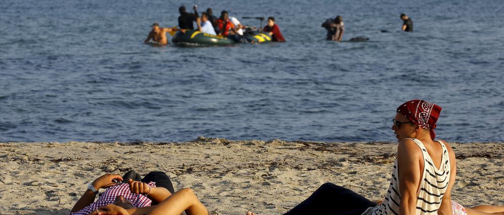 Urlauber liegen am Strand der griechischen Insel Kos, während vor ihnen Flüchtlinge ankommen.