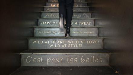 Eine Frau geht eine mit französischen und englischen Sprüchen beschriftete Treppe hinauf. 