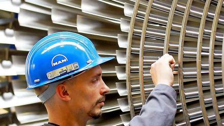 Ein Mechaniker mit blauem Helm arbeitet an den Schaufeln einer Turbine aus Metall.