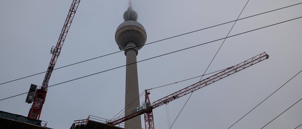  Die Spitze des Berliner Fernsehturms am Alexanderplatz im Bezirk Mitte verschwindet im Nebel, während im Vordergrund eine Baustelle und Baukräne zu sehen sind. 