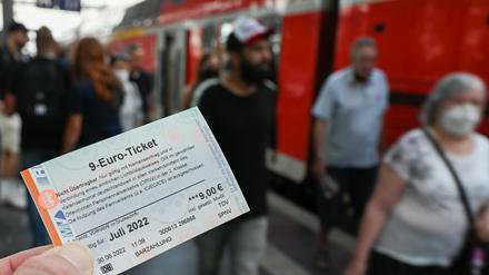 Ein 9-Euro-Ticket für Juli 2022 wird am Hauptbahnhof hochgehalten, während Zugreisende aus einer Regionalbahn aussteigen. 