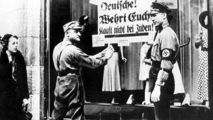 SA-Männer kleben ein Plakat mit der Aufschrift "Deutsche! Wehrt Euch! Kauft nicht bei Juden" an die Schaufensterscheibe eines Geschäfts, das in jüdischem Besitz ist. 
