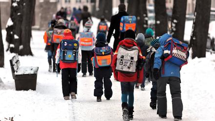 Kinder gehen mit ihren Schulranzen über verschneite Gehwege zu einer Schule in München.